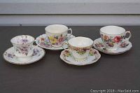 Photo showing four floral teacups and saucers arranged on a dark surface with visible gold accents on rims and handles