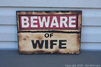 Photo of the rectangular wooden sign with text 'BEWARE OF WIFE', showing burnt edges, natural wood grain, and painted lettering.