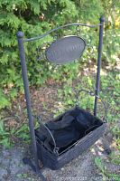 Front angled view of dark wicker basket hanging on black metal stand with 'WELCOME' sign above.