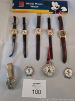 Full display of 9 Mickey Mouse watches laid flat including 5 on leather bands, 1 on metal stretch band, 3 without bands including a large silver pocket watch