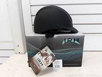 Black IRH riding helmet with ventilation slots placed on its original branded box alongside informational tags and a lot number card.