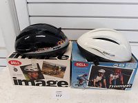Two Bell bike helmets displayed with their original boxes, one black Image model and one white Triumph model