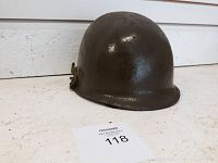 Front left side view of olive green military helmet on white surface showing metal shell and chin strap.