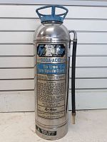 Photo showing full view of Fyrite soda acid fire extinguisher, silver metal body with blue handle and attached hose.