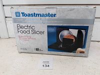 Front and top view of Toastmaster Electric Food Slicer box showing product name, image of slicer with sliced meat, and product features in red box.