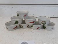 Front view of 8 white porcelain ramekins arranged in two rows showing vegetable illustrations