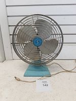 Front view of Superior Electric blue metal table fan showing cage, blades, and power cord