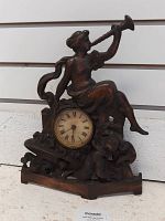 Front view of antique figurine table clock showing woman blowing a horn and cherub figure with clock face below.