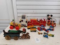 Full lot view showing various Disney toys including Mickey and Minnie Mouse figures, robot toy, vintage cars, trucks, red toy train engine, and cast iron horse-drawn wagon figurines.