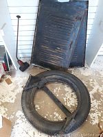 Metal car hood leaning against wall with vent slats showing, spare tire on rim with crossbar on floor in front