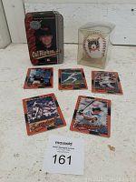 Photo of the full lot including a metal collector's tin box with Cal Ripken Jr. image, a commemorative baseball in plastic display case, and five Metallic Impressions baseball cards laid out.