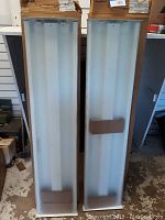 Front view of two fluorescent ceiling light fixtures with diffuser covers visible, placed side by side on floor.