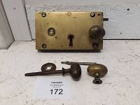 Wide view of antique brass lock plate with keyhole, small round knob, and accompanying hardware on table.