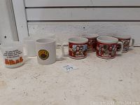 Photo of 8 white mugs including 4 Campbell's soup mugs, 1 Starbucks mug with logo, and 3 milk glass mugs with cartoon designs.