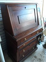 Front and side view of the antique wooden writing desk showing slant front and brass knobs on drawers.
