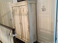 Full side and front angle view showing distressed white painted armoire with carved details