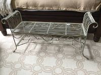 Full view of the wrought iron bench showing slatted seat, curved armrests, and scroll detail on the sides and legs.