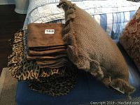 Assorted folded bedding items including leopard print cloth and tan textured pillow with braided trim
