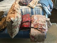 Photo showing floral throw pillow and folded bedding including sheets with floral patterns on a bed.