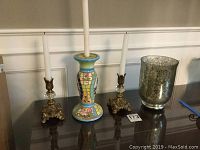 Wide shot of all four items on a reflective wooden surface showing the candlestick holders and candle holder together.