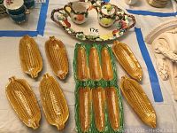 Ceramic corn on the cob dishes with detailed kernels and green husks, arranged around a central larger corn dish.
