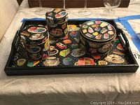 Tea party tray and four round decorative tins with colorful cake and tea-themed designs on black background.