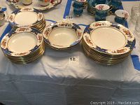 Full view of the dinner service plates, bowls, and other items laid out on a table with floral and cobalt blue gold-trimmed patterns.
