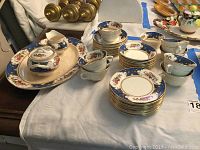 Photo shows entire tea set including cups, saucers, dessert plates, sugar bowl, creamer, and platter arranged on white cloth.