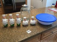 Wide shot of all items including condiment containers, teapot, glass jar, and Sterilite bowl on kitchen counter.