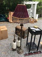 View of one floor lamp with decorative burgundy velvet lampshade with gold fringe, and two matching 26-inch table lamps with white ceramic and brass bases shown outside among other items.