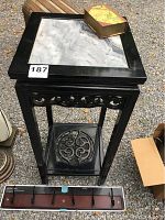 View of black wooden side table with white marble inset top, decorative carved details, and bottom shelf with carved circular panel. Wooden coat rack with five hooks placed in front.