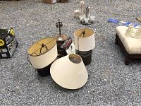 Three table lamps with shades on gravel ground, showing lamp bases and fabric shades. Varied lamp shade shapes visible.