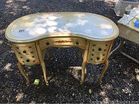 View of the entire kidney-shaped vanity desk showing the cream color, ornate drawer pulls, curved legs, and overall condition including scratches and wear on the surface.
