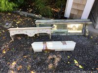 Four different floating wall shelves including one large shelf with a mirror backing, two white shelves with floral decoration, and one wrapped white shelf section; displayed outside on gravel.