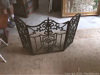 Full view of the three-panel vintage wrought iron fireplace screen showing mesh center and decorative floral and scroll work.