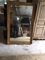 Full view of the large rectangular mirror leaning against a wall in a garage setting with the photographer’s reflection visible.