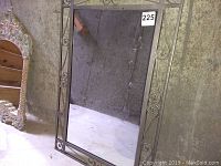 Rectangular vintage mirror with dark metal frame and scrollwork decoration leaning against a wall.