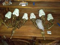 Pair of brass wall sconces with two arms each and white fabric lampshades, viewed from above on wooden surface.