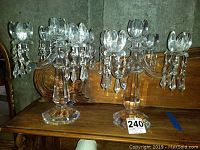 Pair of clear crystal candle holders with ornate cut facets and hanging crystal drop prisms on wooden surface.