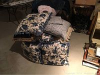 Seven decorative pillows stacked showing blue floral pattern and beige geometric pattern pillows with fringe and crochet details.