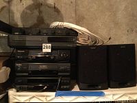Stack of audio and video equipment including Panasonic VHS player and two speakers, showing overall condition and components in the lot.