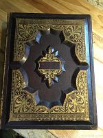 Front cover showing ornate dark brown leather with gold embossed decorative elements and raised center design.