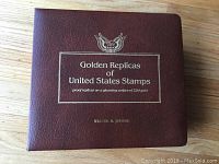 Brown leather-bound album with gold embossed title and eagle emblem saying 'Golden Replicas of United States Stamps proof replicas on a gleaming surface of 22kt gold'
