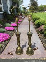Full view of two brass Stiffel lamps outdoors on stone walkway with a garden background, showing overall height and shape.