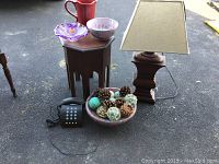 Photo showing octagon end table with items on it including a lamp, a decorative bowl with potpourri, and a phone placed on the ground next to it.
