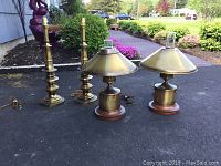 Both brass hurricane lamps with wood bases and enamel-lined cone-shaped shades on pavement outdoors.