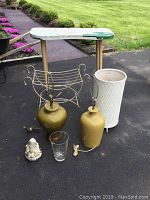 Photo showing dressing table with gold legs, iron bench, two ceramic base lamps in mustard yellow, clear bubble vase, white wicker hamper and Blessed Mother statue.