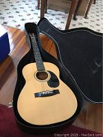 Full view of Hohner acoustic guitar inside open hard shell case showing natural wood body and black pickguard.