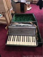 Accordion in open case on a red carpeted floor, showing the full piano keyboard and straps.