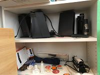 Sony iPod dock system with two satellite speakers, subwoofer, Pamex binoculars, travel iron, vintage pins, and extension cords on shelf